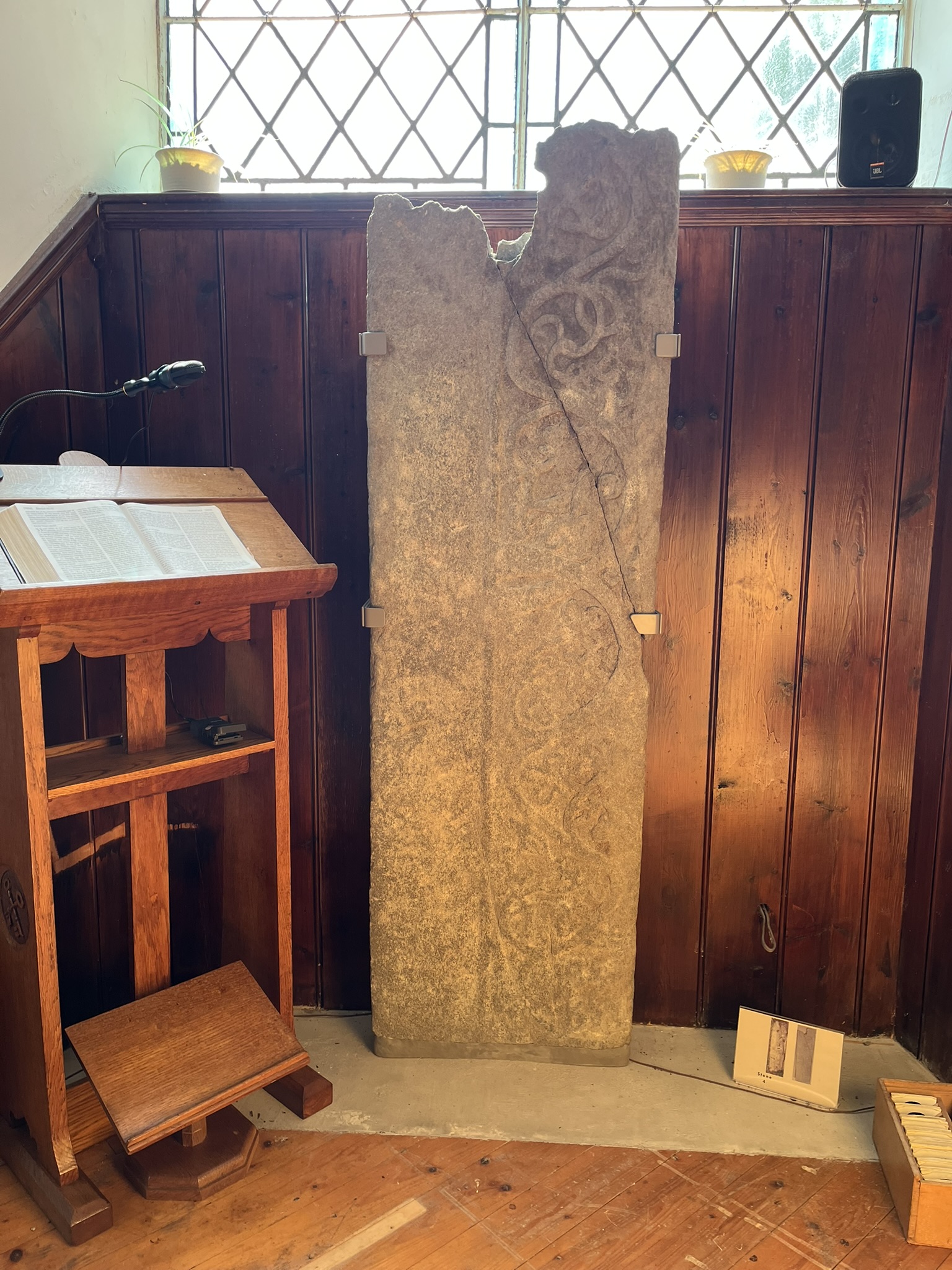 A long grave-slab carved with a running pattern of foliage, propped against the panelling beside the church lectern.