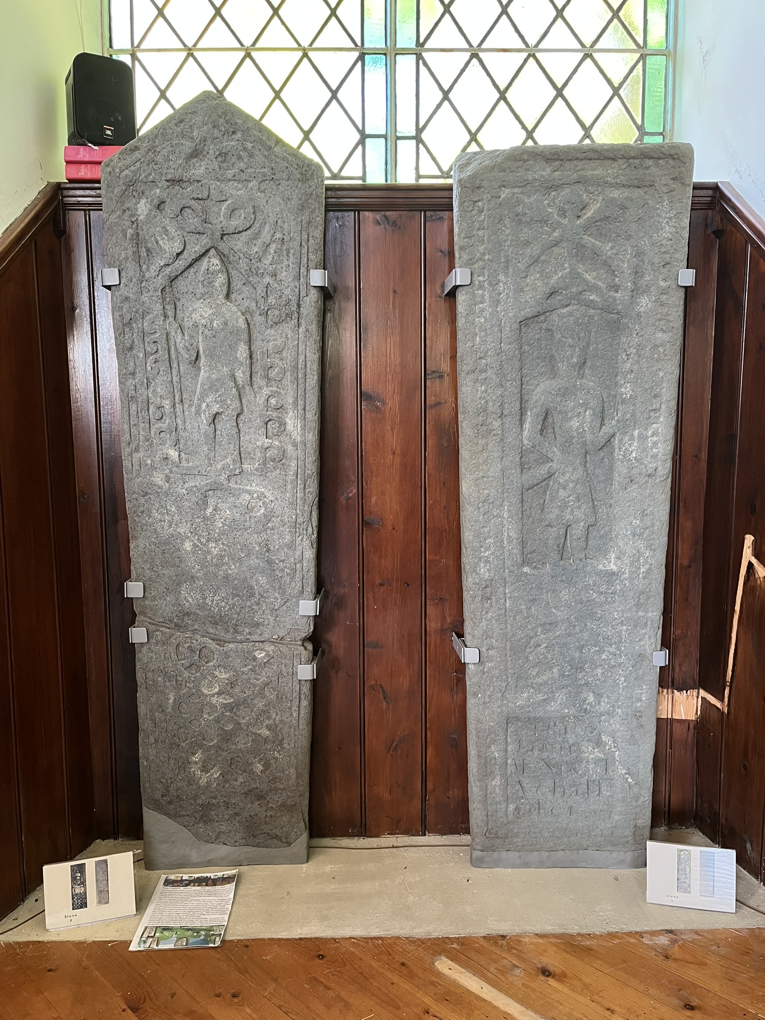 Two tall medieval grave-slabs standing upright against the wood panelling inside Glenorchy Parish Church, each carved with a standing armed warrior figure.