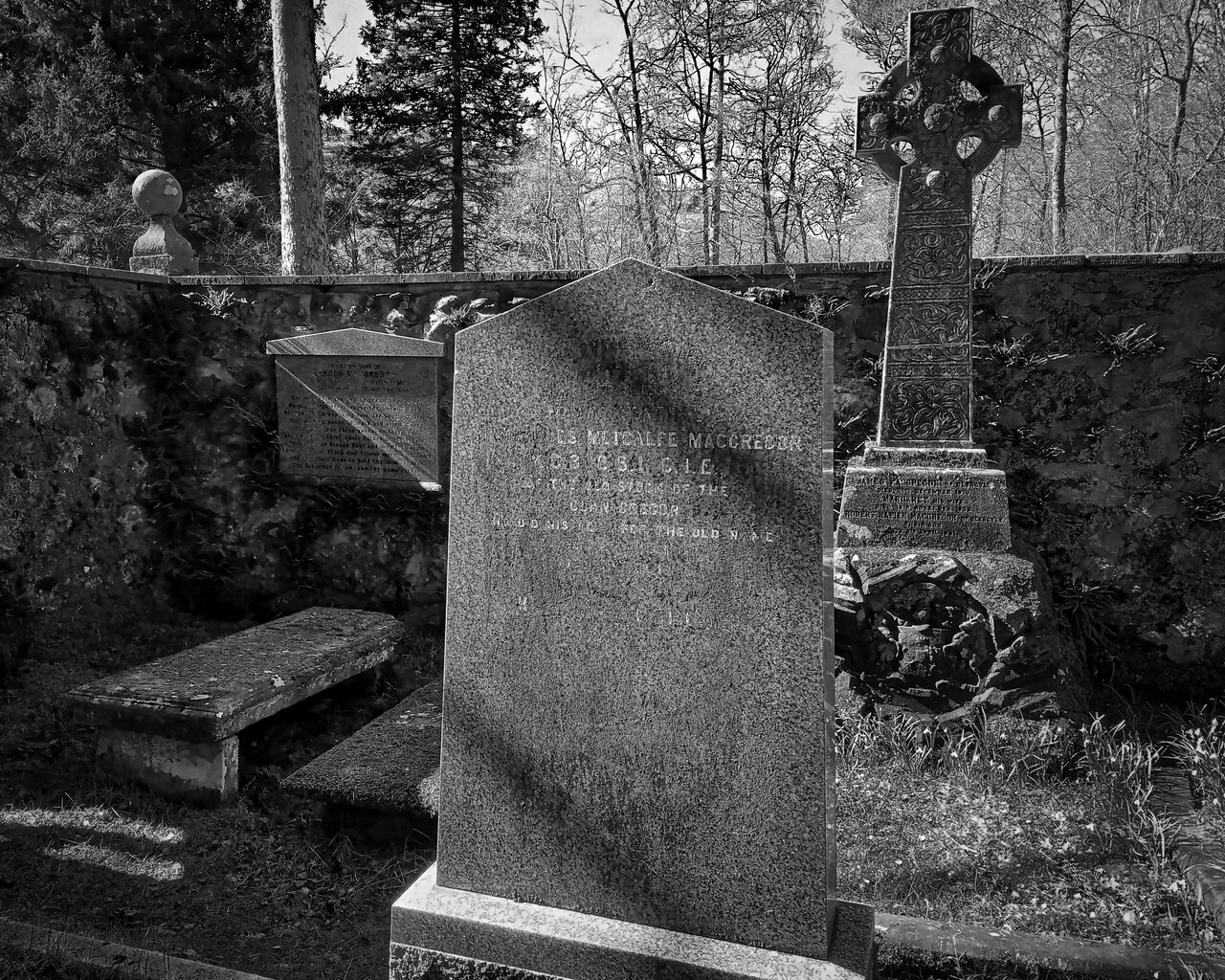 Black and white photograph inside the burial enclosure, showing a plain headstone in the foreground, a Celtic-cross memorial to its right, and a smaller inscribed slab against the left-hand wall.