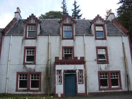 Glengyle House seen head-on: a harled, white-rendered three-bay house with red-painted margins, crow-stepped gables and dormer windows, and a stone-surrounded front door beneath a carved lintel.