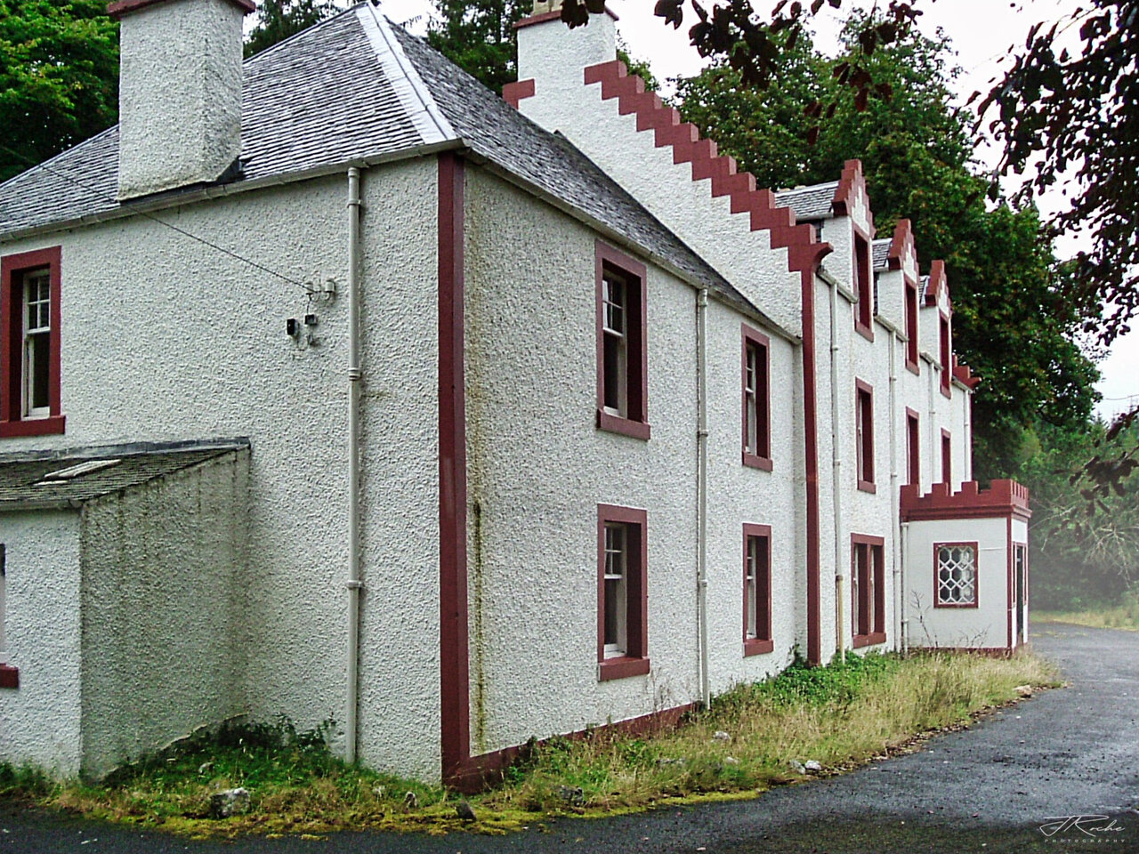 Glengyle House from the west, showing the gable end with its chimney and the long flank of the building stretching away towards the later eastern wing, which carries an oval oeil-de-boeuf window.