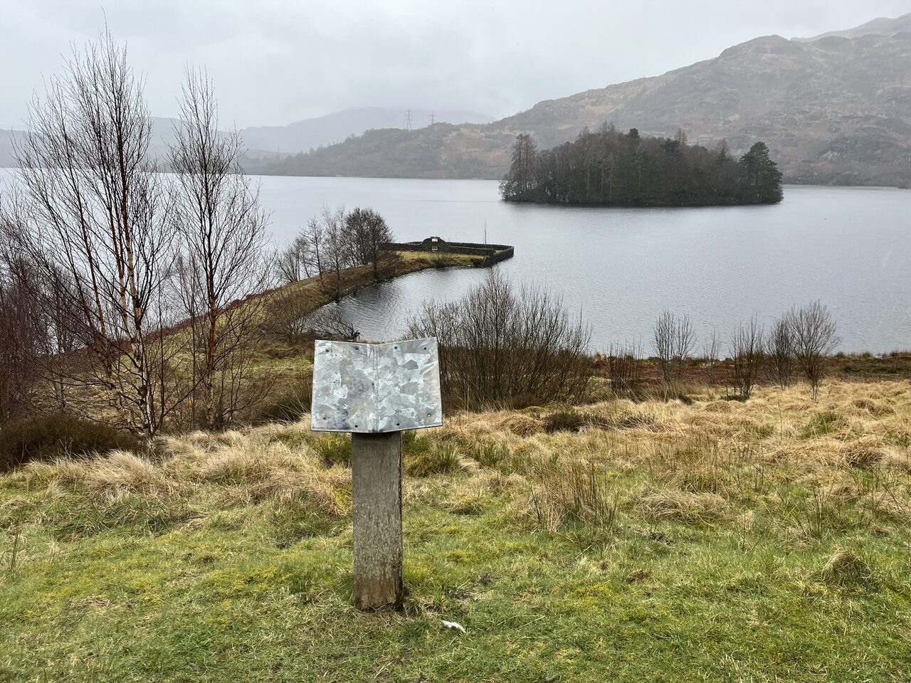 The T-shaped causeway carrying the Portnellan burial ground out into Loch Katrine, viewed from higher ground beside the lochside path.