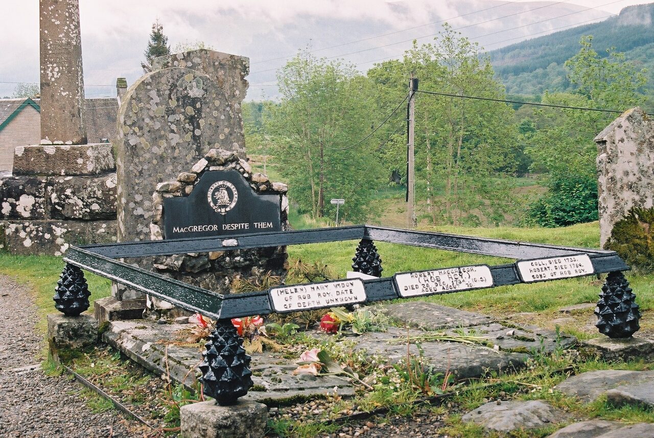 Rob Roy MacGregor's grave at Balquhidder old parish church: three side-by-side stone slabs within iron railings, the centre stone carved with the motto 'MacGregor Despite Them.'