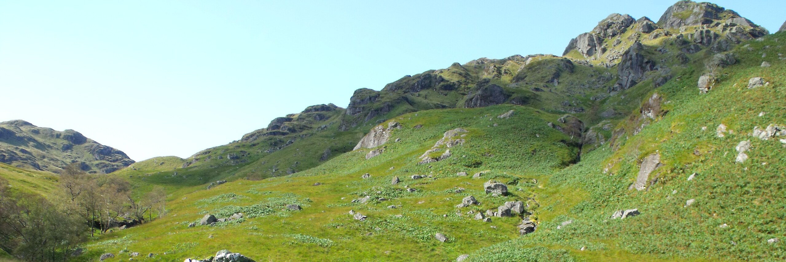A weathered grouping of rocks on a knoll above the ruin of a stone building in Glen Gyle, with the rough grass and ferns of the glen falling away beyond.